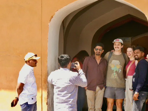 Tourists taking a group photo near a historic building's archway in a sunny outdoor setting in india