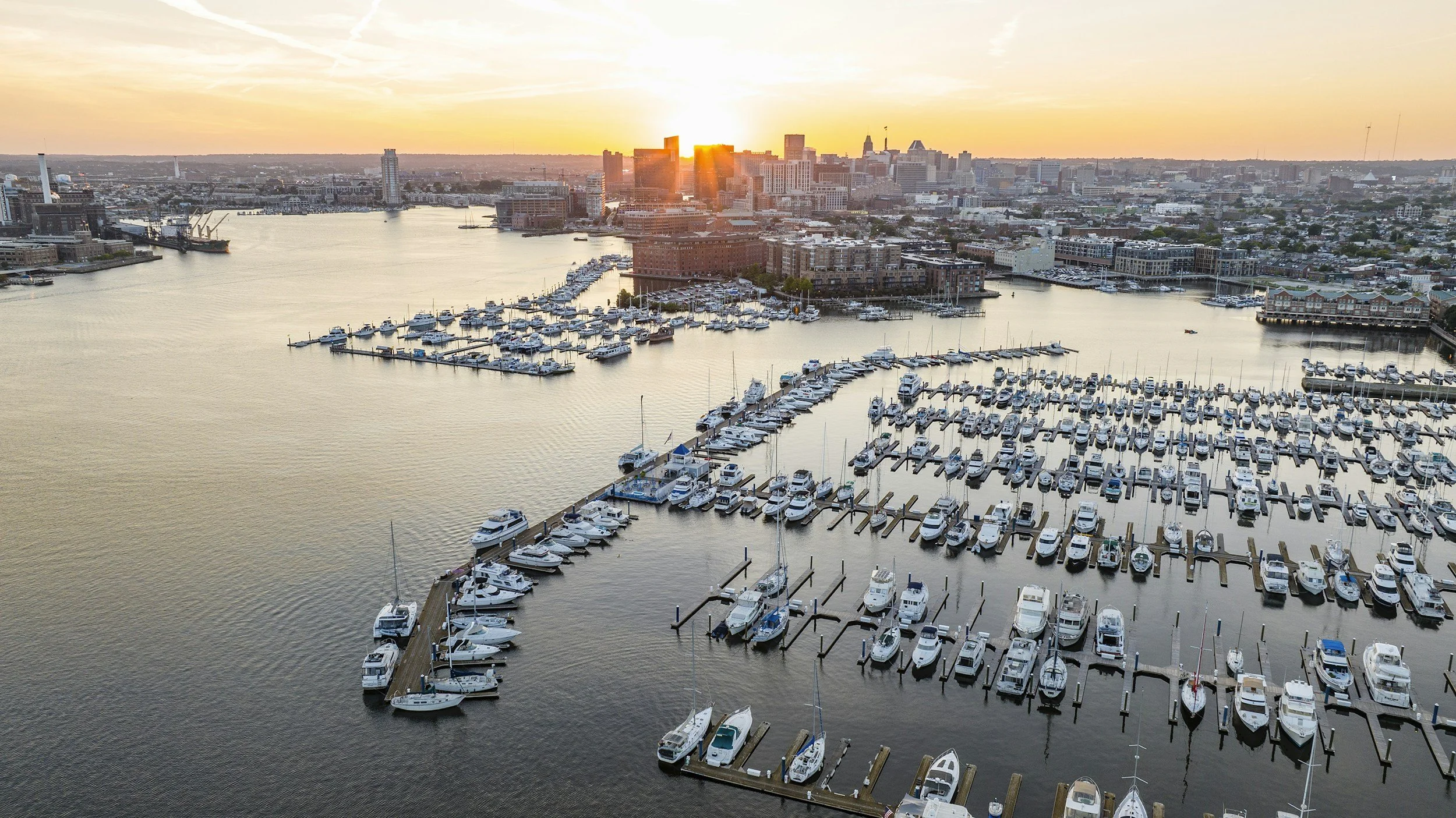 Aerial view of a marina filled with boats during sunset in a city with tall buildings.