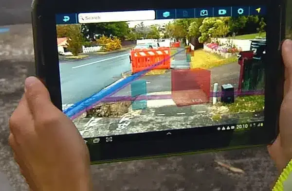 Person holding a tablet showing a traffic camera view of a street with an orange construction barrier and some orange and purple safety fencing.