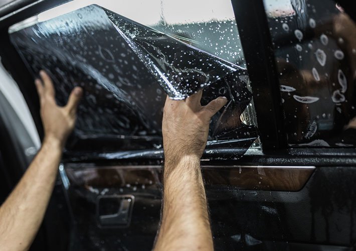 Someone applies a protective film or tint to a vehicle's window.