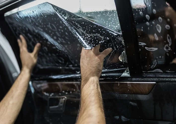 Person installing or replacing window tint film on a car window.