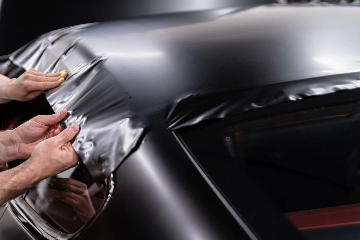 Two hands apply black protective film or tint to a car's rear window.