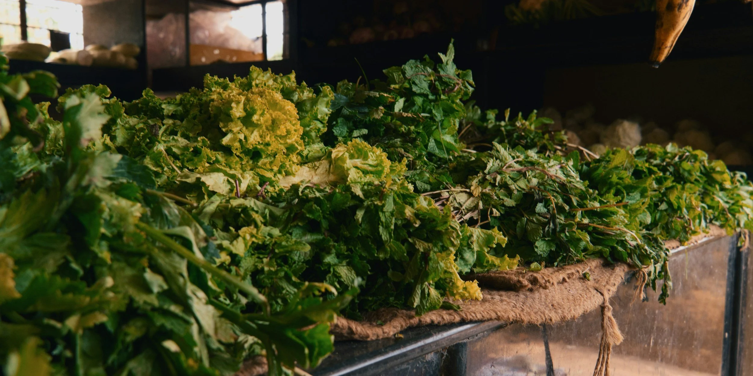 Variety of fresh green leafy vegetables arranged on a table inside a rustic kitchen.