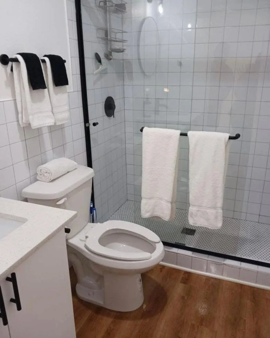 Bathroom with a toilet, a glass shower enclosure with white towels hanging on a black towel bar, and white tiles on the walls.