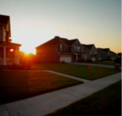 Residential neighborhood at sunset with houses, a sidewalk, and a lawn.