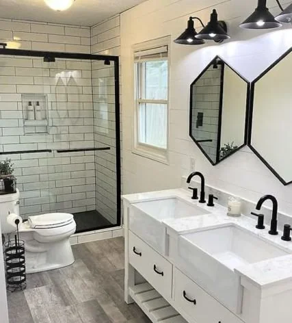 Modern bathroom with a glass shower enclosure, a toilet, a white double vanity with black fixtures, hexagonal mirrors, and black wall-mounted light fixtures.