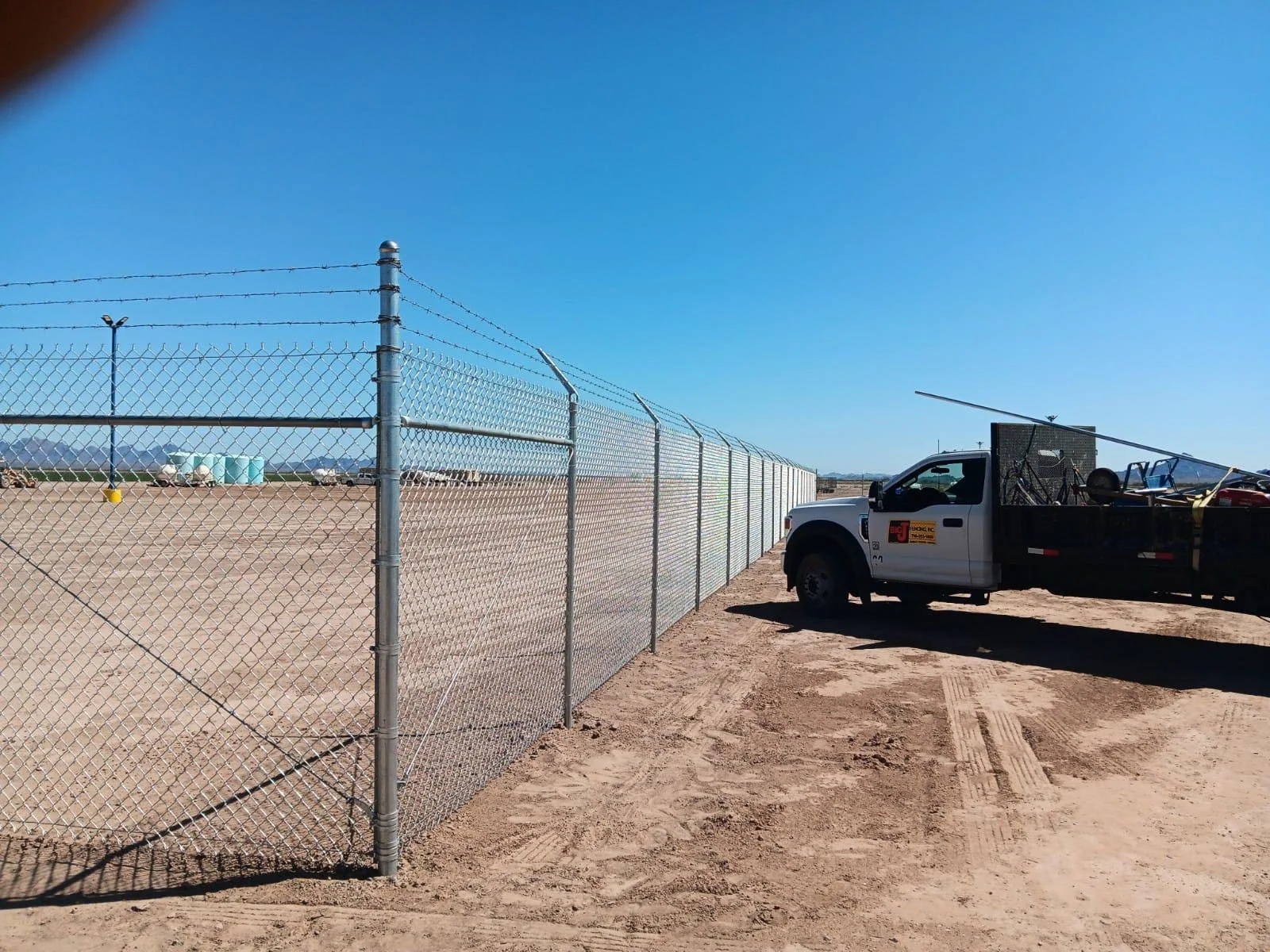 A fenced area with a white utility truck parked beside it, on a dirt surface under a clear blue sky.