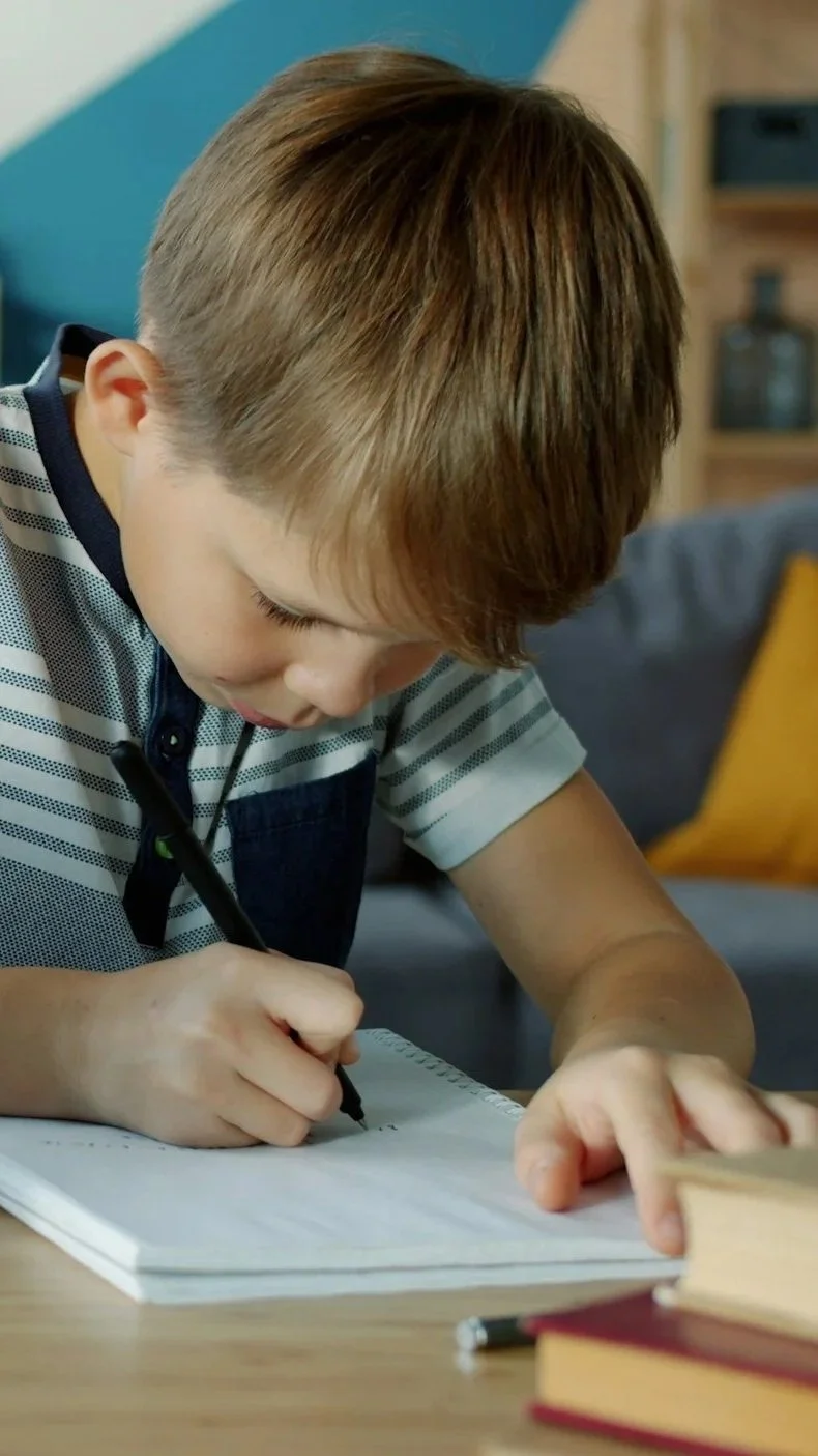 A young boy with brown hair writing in a notebook.