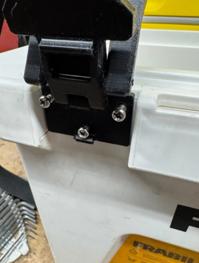Close-up of a black clamp attached to a white piece of equipment, with screws securing the clamp.