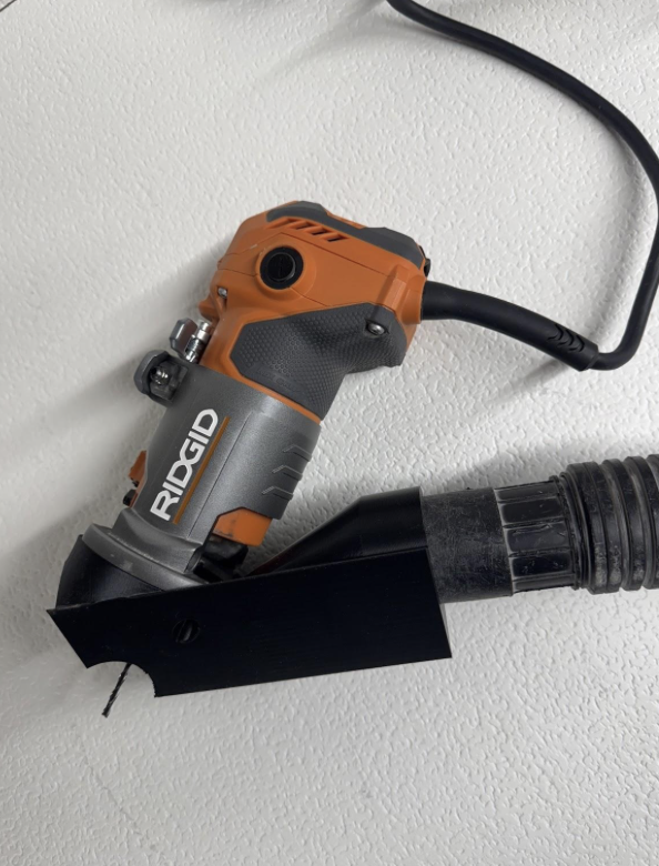An orange and black handheld power drill attached to a black hose on a white textured wall.