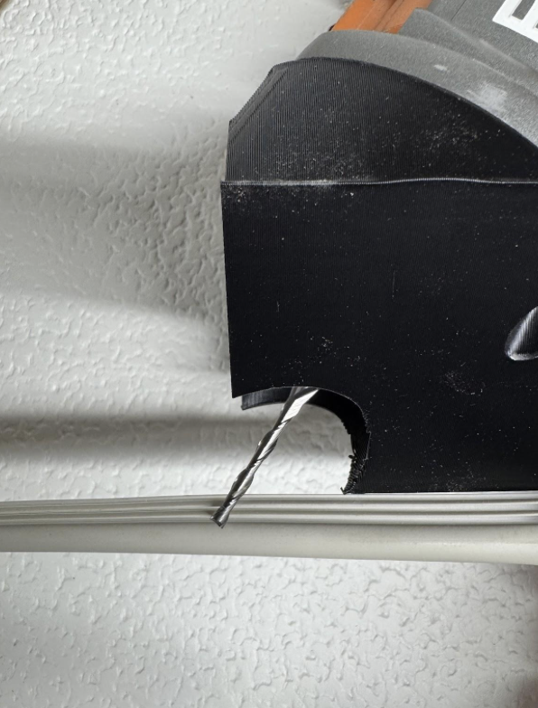 Close-up of a power drill with a drill bit, attached to a black, wall-mounted tool holder, with a metal rail below, against a textured white wall.