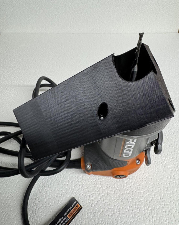 A woodworking router placed on a white textured surface with a black plastic protective cover and power cord.