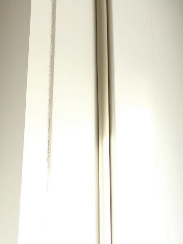 Close-up of a door frame with two vertical white door hinges.