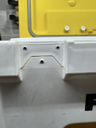 Close-up of a white plastic object with three small holes and a thin metal wire.