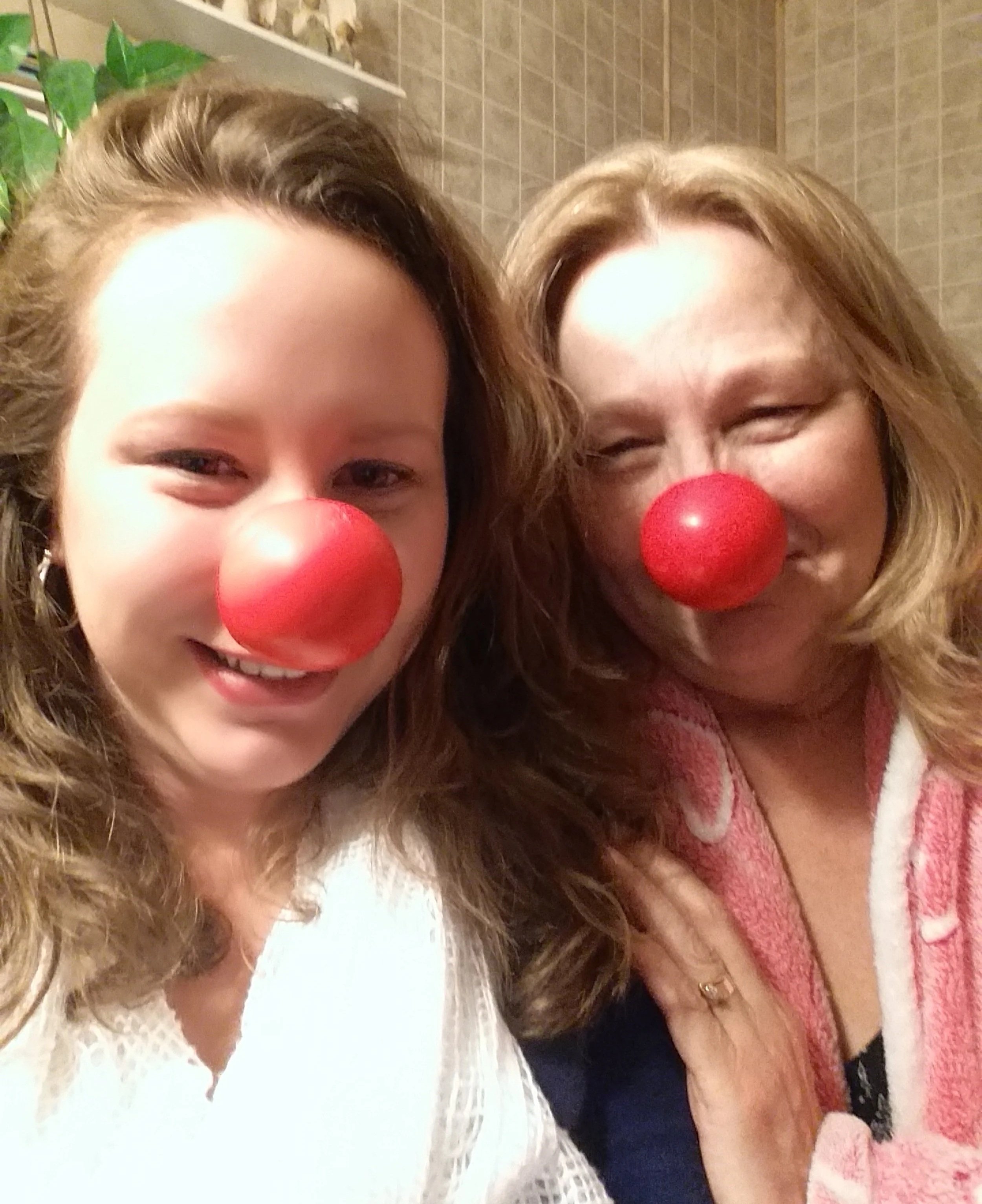 Two women wearing red clown noses and smiling for a selfie.