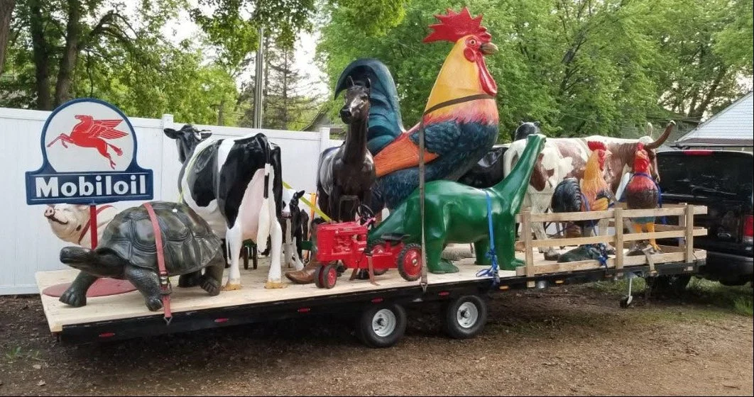 A parade float with various animal sculptures including a turtle, cow, horse, rooster, green dinosaur, and other farm animals, along with a Mobil oil sign, on a wooden platform attached to a trailer.