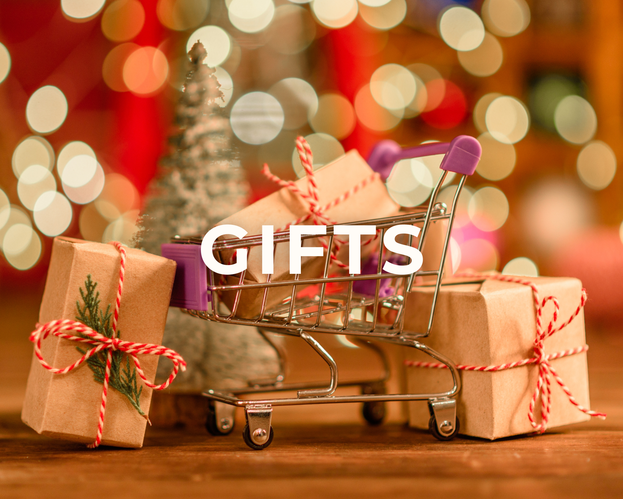 A small shopping cart filled with wrapped Christmas gifts with red and white string, placed on a wooden surface. In the background, there are blurred colorful lights, creating a festive holiday atmosphere.