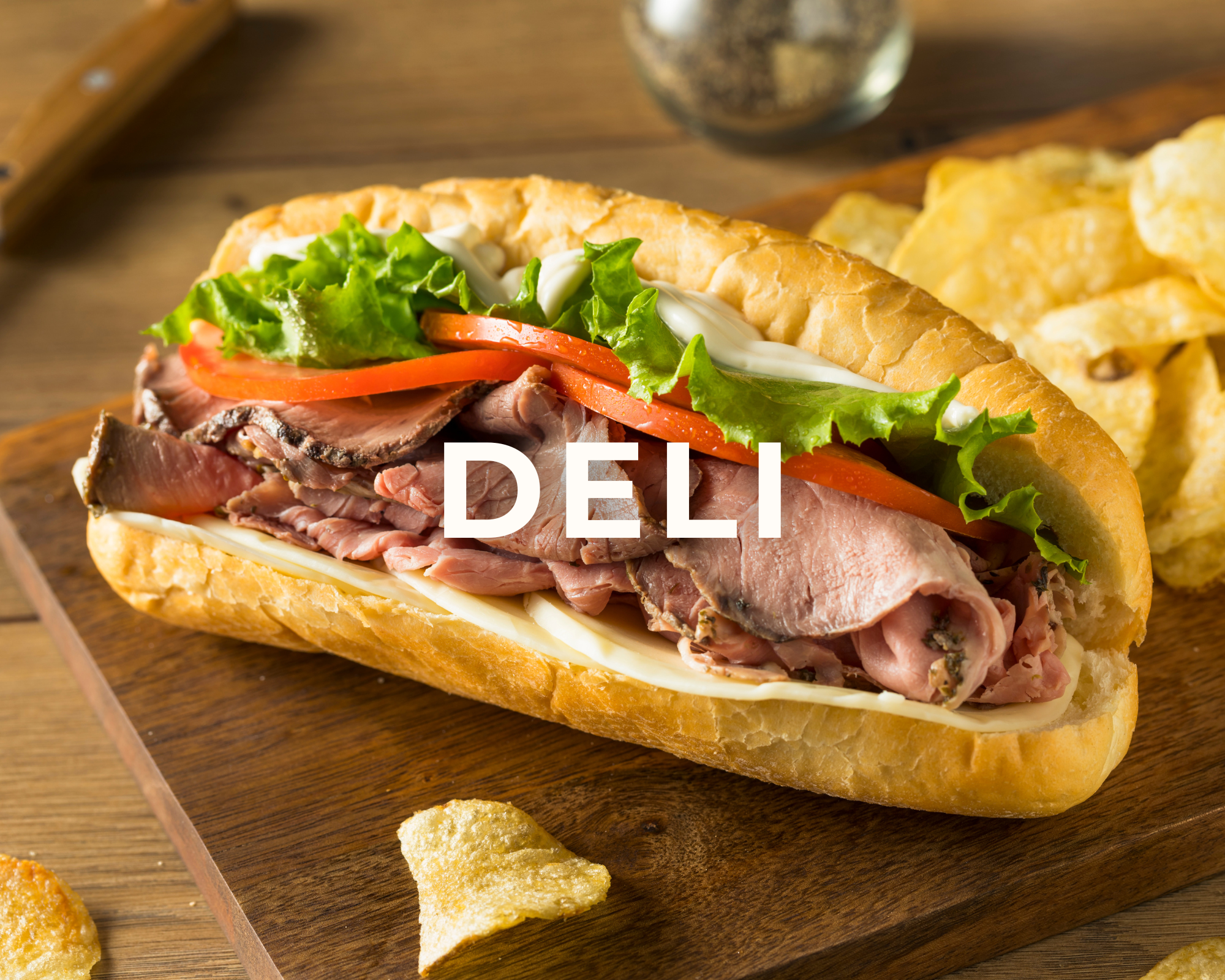 Sub sandwich with roast beef, lettuce, tomato, cheese, and mayonnaise on a wooden tray, with potato chips in the background.