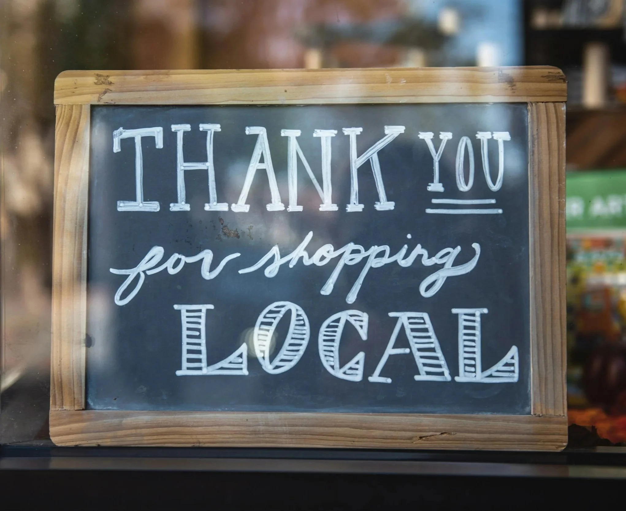A chalkboard sign with a wooden frame that reads 'Thank you for shopping local' in white handwritten letters.