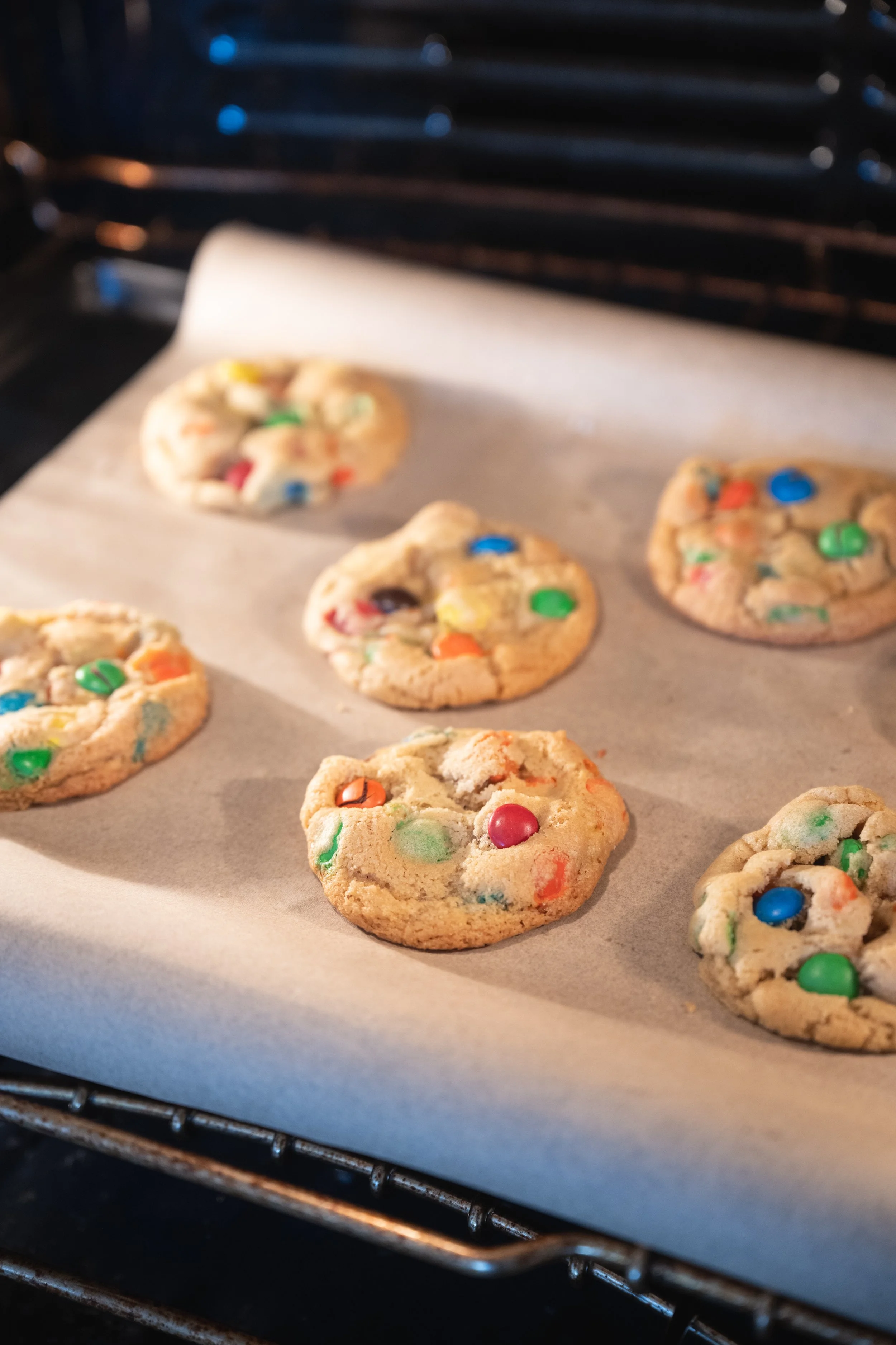 Cookies with colorful M&M candies on a baking sheet in an oven.