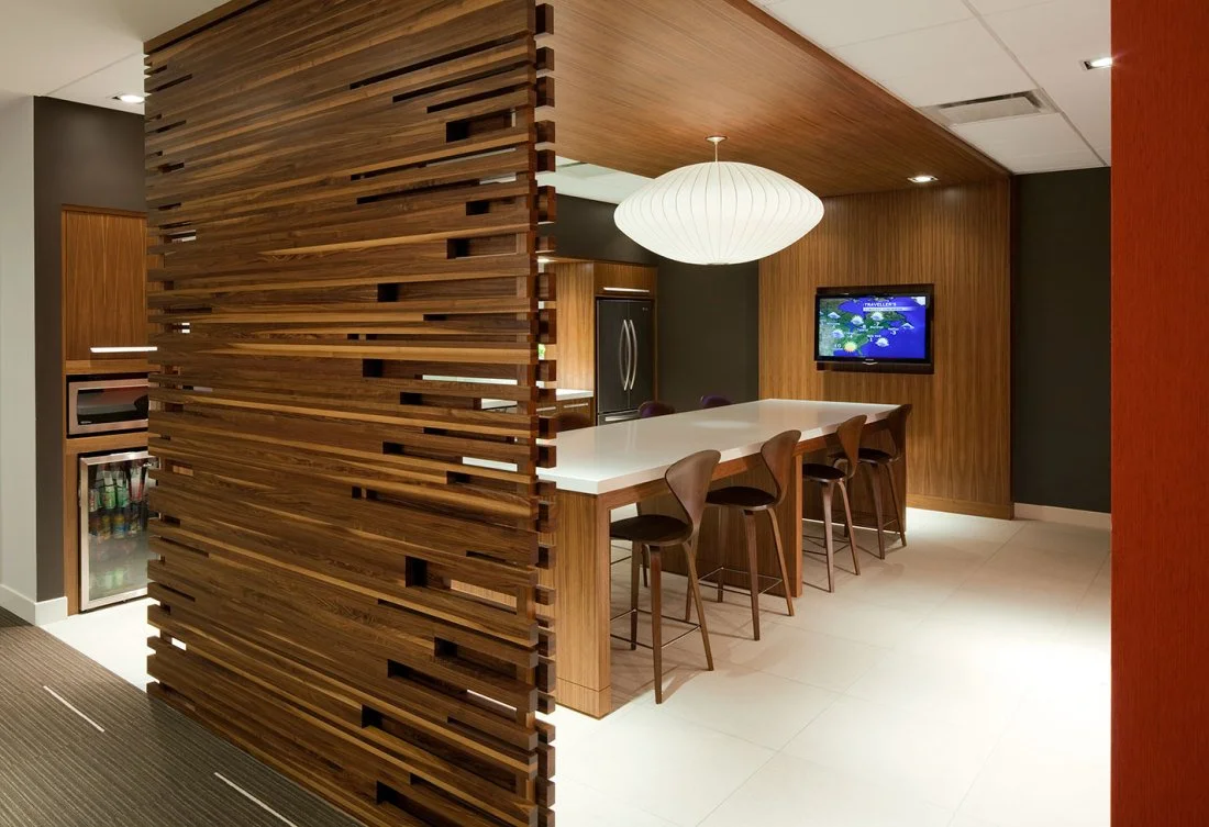 Modern kitchen with wooden slat room divider, white island counter, bar stools, a TV on the wooden wall, and a white pendant light.