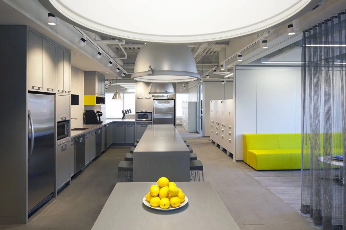 Modern office kitchen with gray cabinets, stainless steel appliances, large kitchen island, and a lounge area with yellow seating