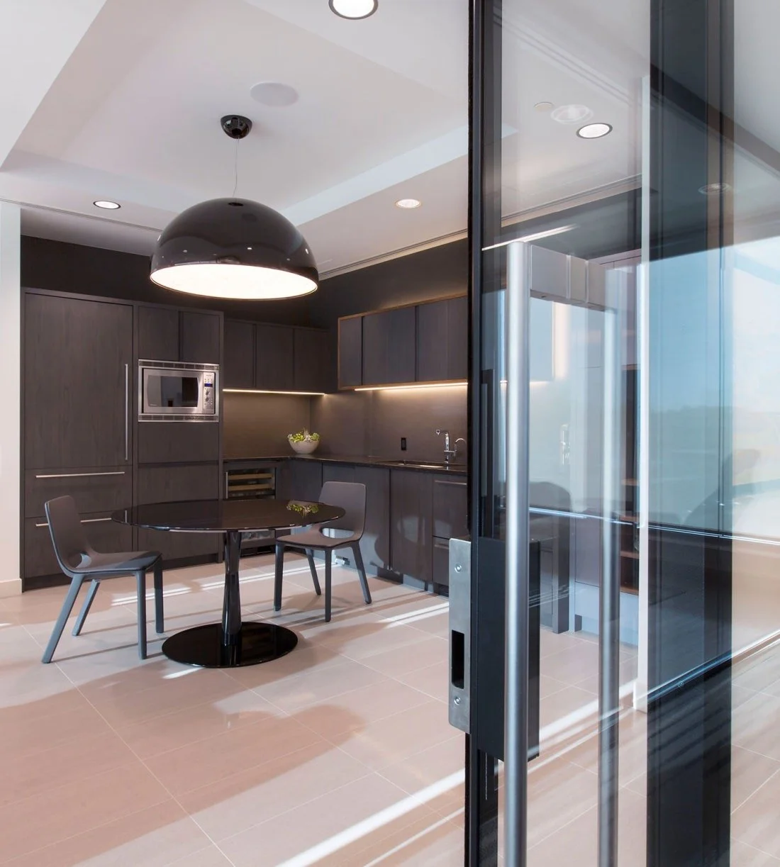 Modern kitchen with dark cabinets, a black dining table, three gray chairs, a microwave, and sliding glass doors.