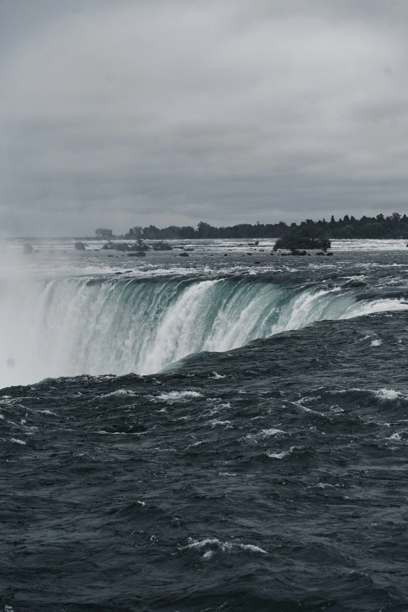 A waterfall with water cascading over the edge, surrounded by dark water and overcast skies