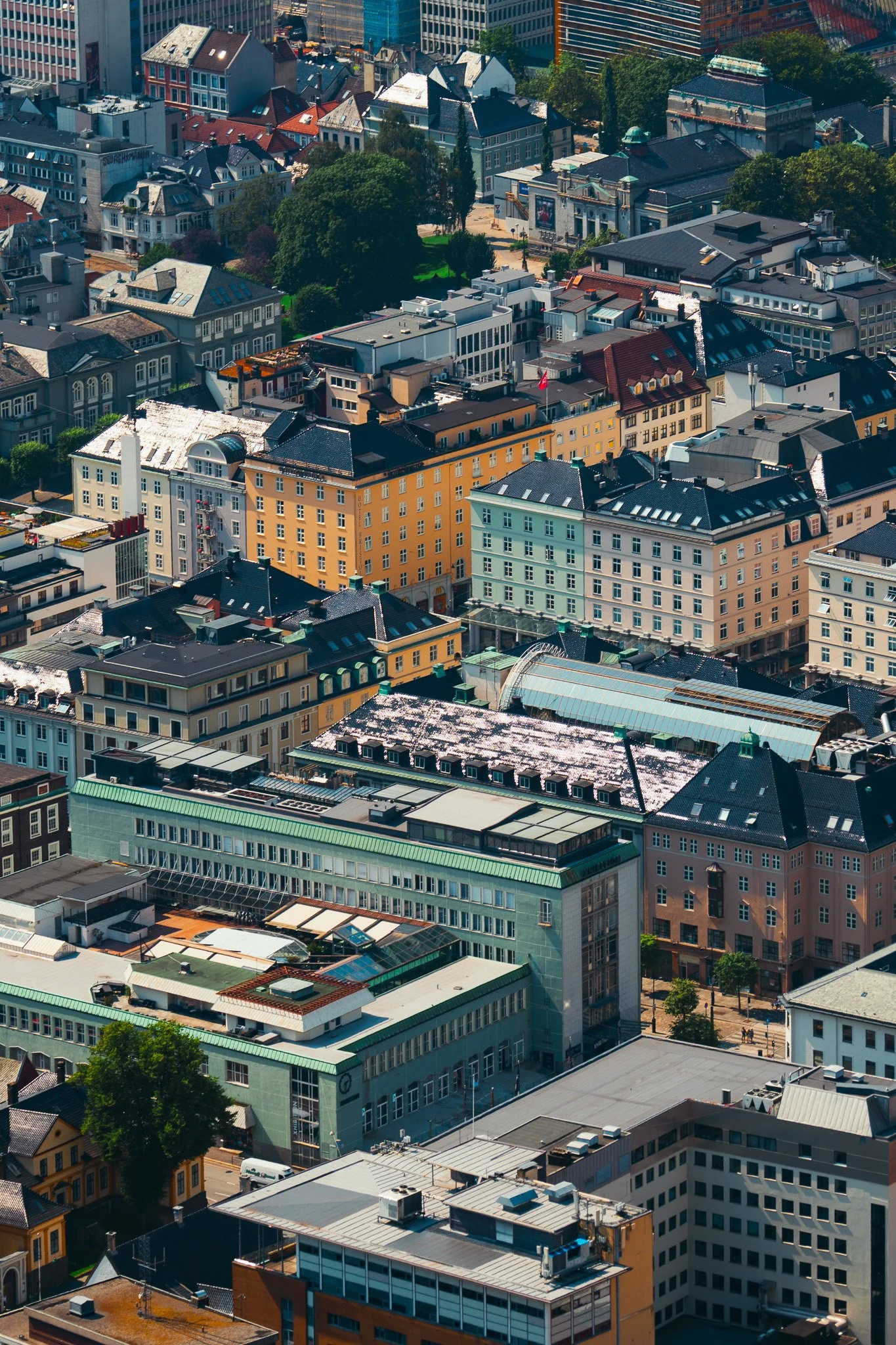 Aerial view of a cityscape with various colored buildings, including yellow, gray, and white structures, along with some green rooftops and trees interspersed among the buildings.