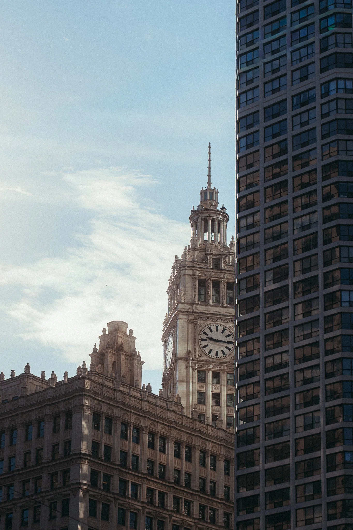 View of a historic clock tower building framed by a modern glass skyscraper in an urban cityscape.