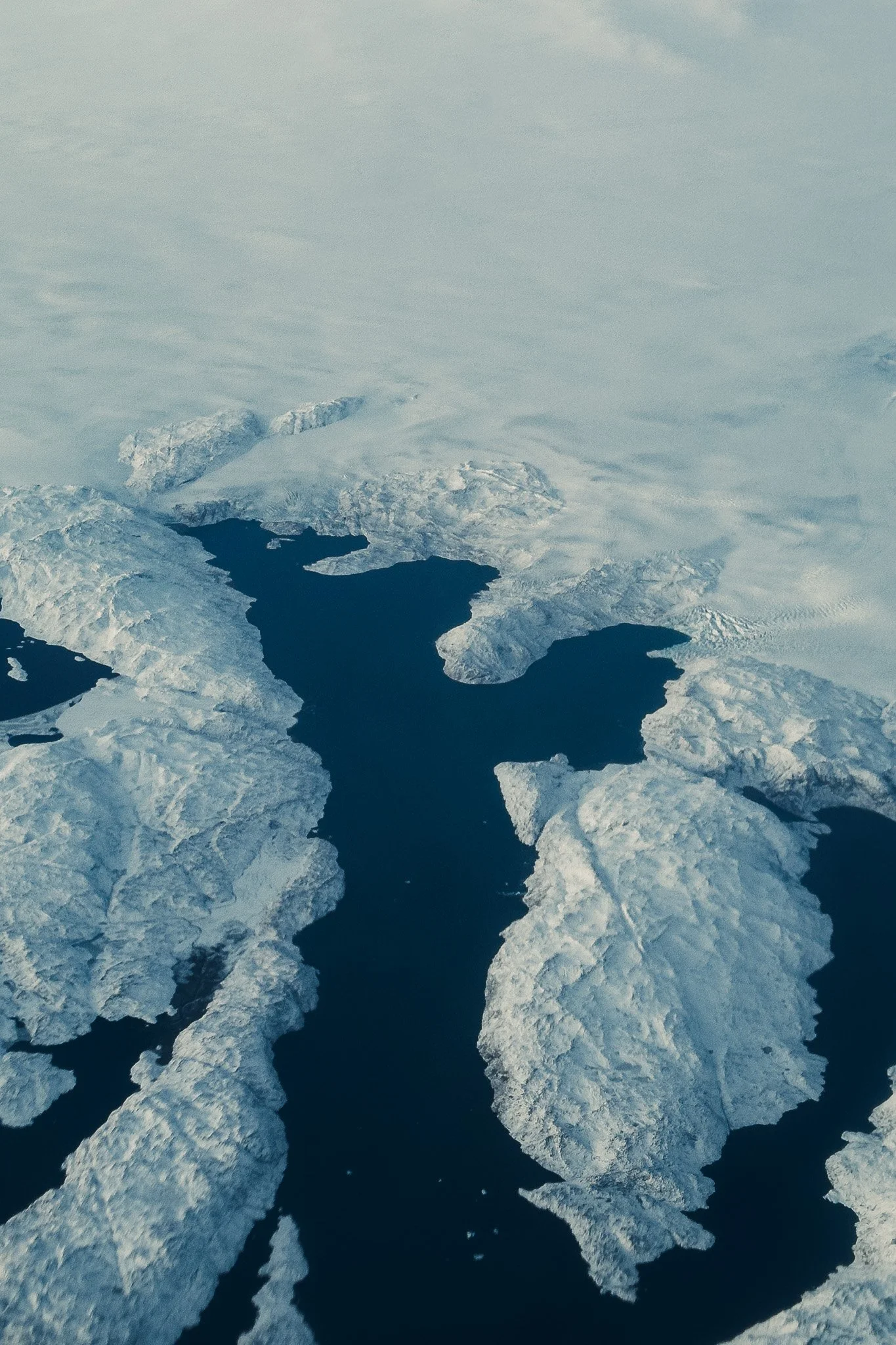 Aerial view of icy Arctic waters with open sea water surrounded by floating ice sheets and icebergs.