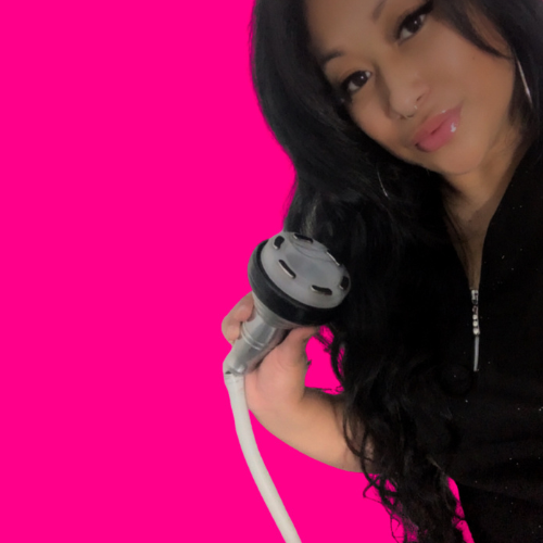 Young woman with long black hair holding a black and silver hairdryer against a bright pink background.