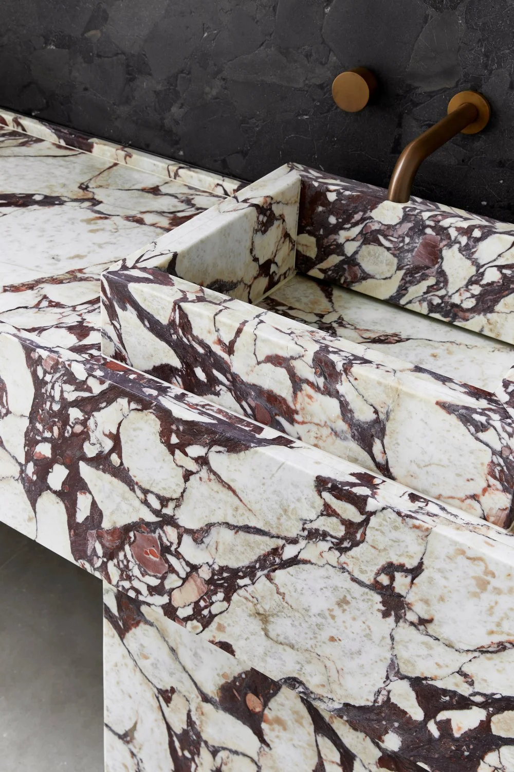 Close-up of a marble sink and countertop with a brass faucet and black marble backsplash.