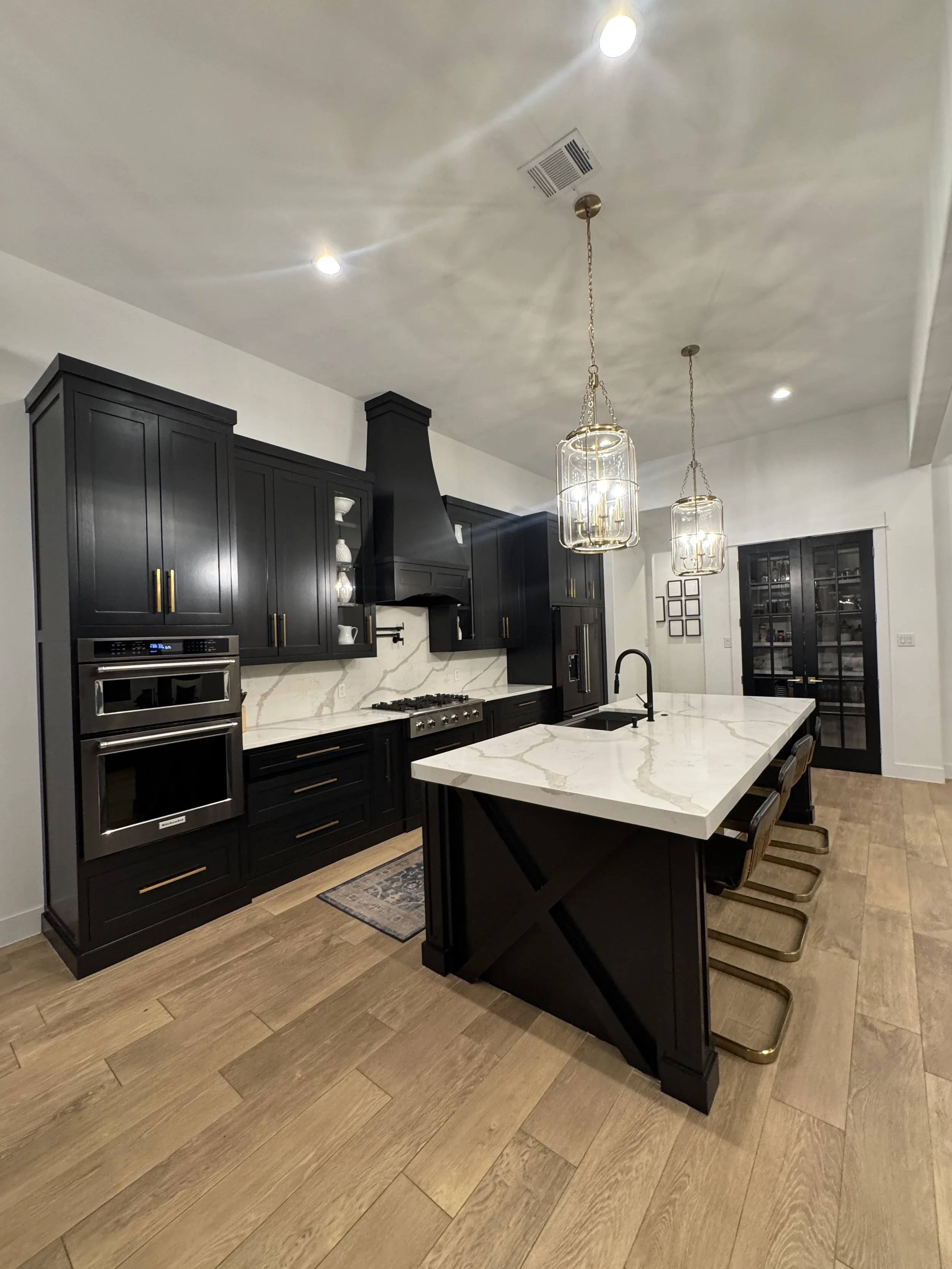 Modern custom home with black cabinets, brand new large white marble island, pendant lights, stainless steel appliances, and wood flooring in Dallas, Tx