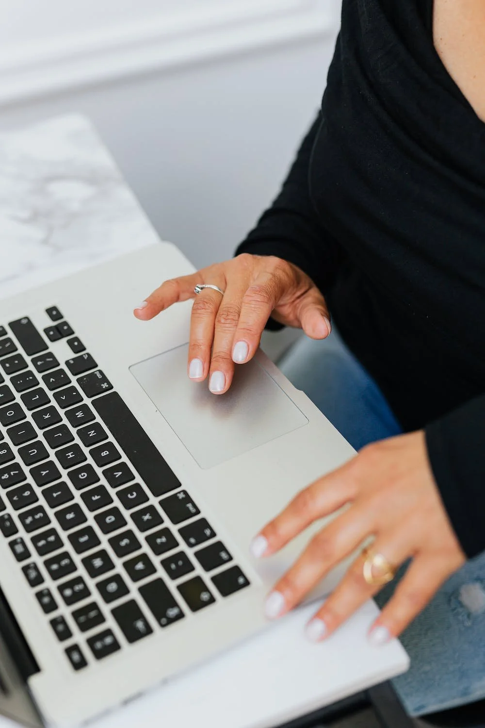 Person wearing a black shirt using a silver laptop with a marble surface nearby.