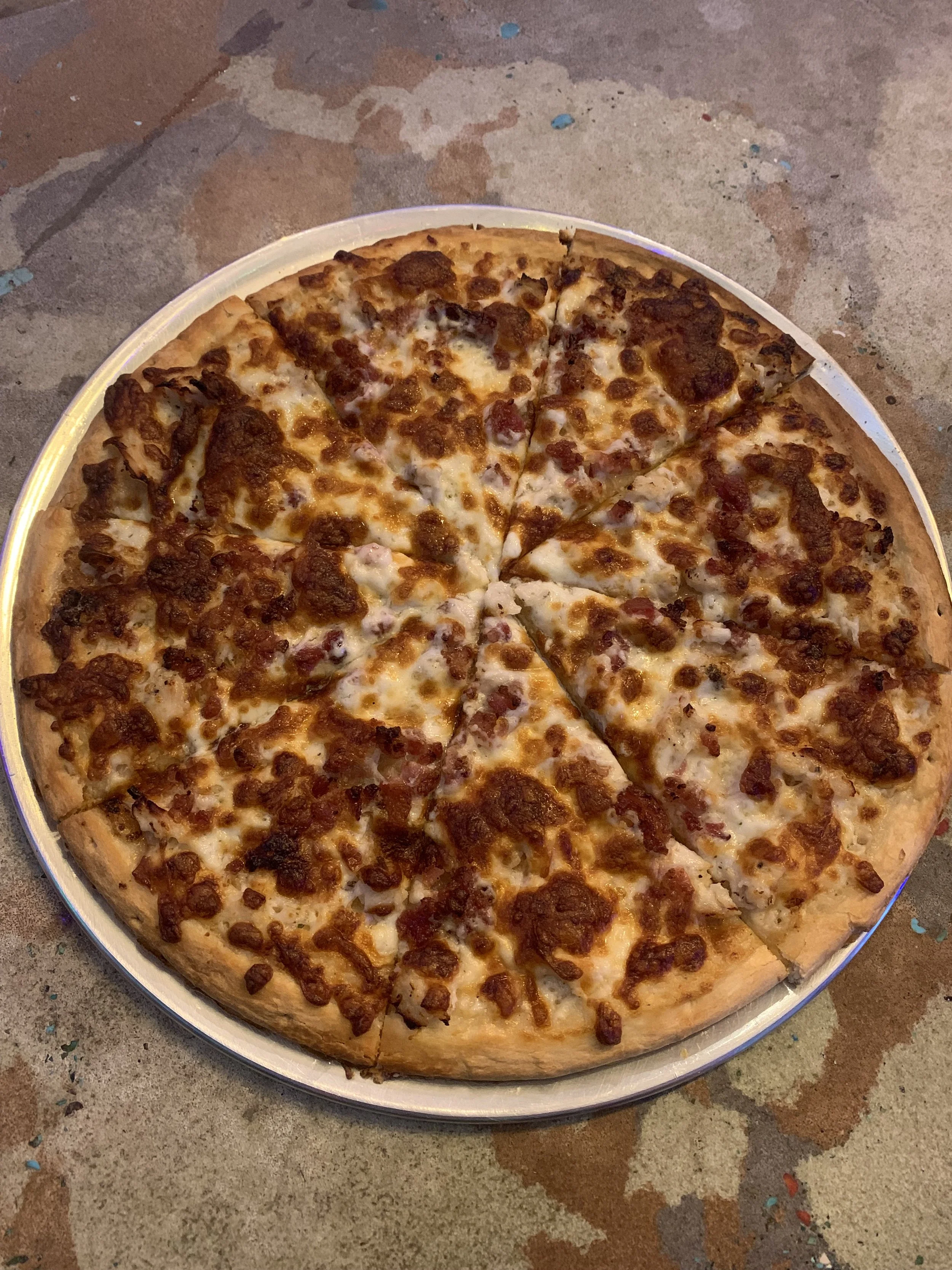 A large cheese and pepperoni pizza with a golden crust on a round tray on a concrete table.