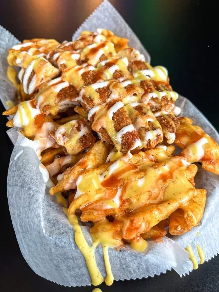 A basket of loaded fried chicken tenders topped with various sauces and drizzles on parchment paper.