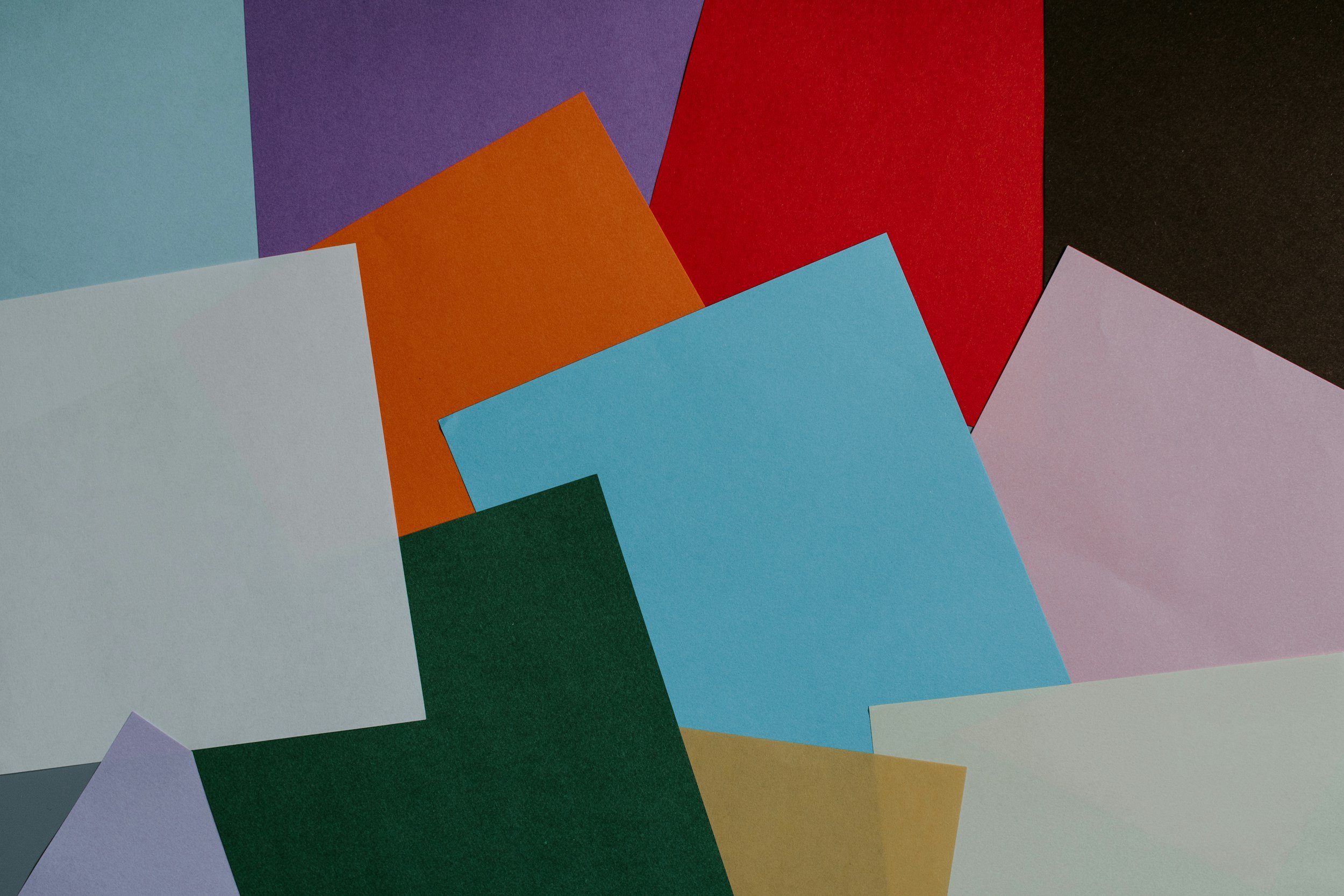Colorful construction paper sheets overlapping each other, including blue, green, orange, red, purple, black, pink, white, gray, and tan.