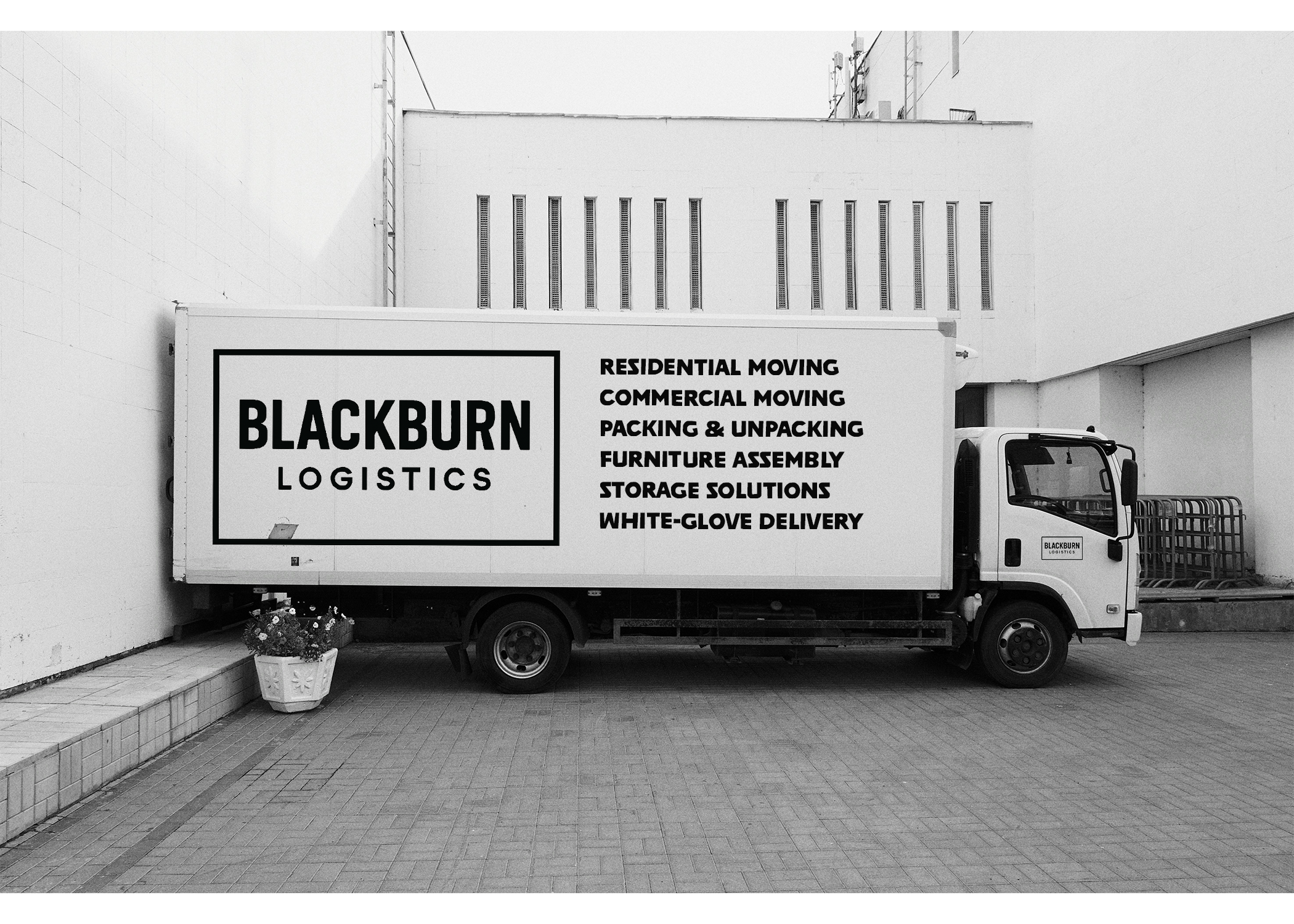Blackburn Logistics moving truck parked against a white building with a potted plant nearby and a list of logistics services written on the side.