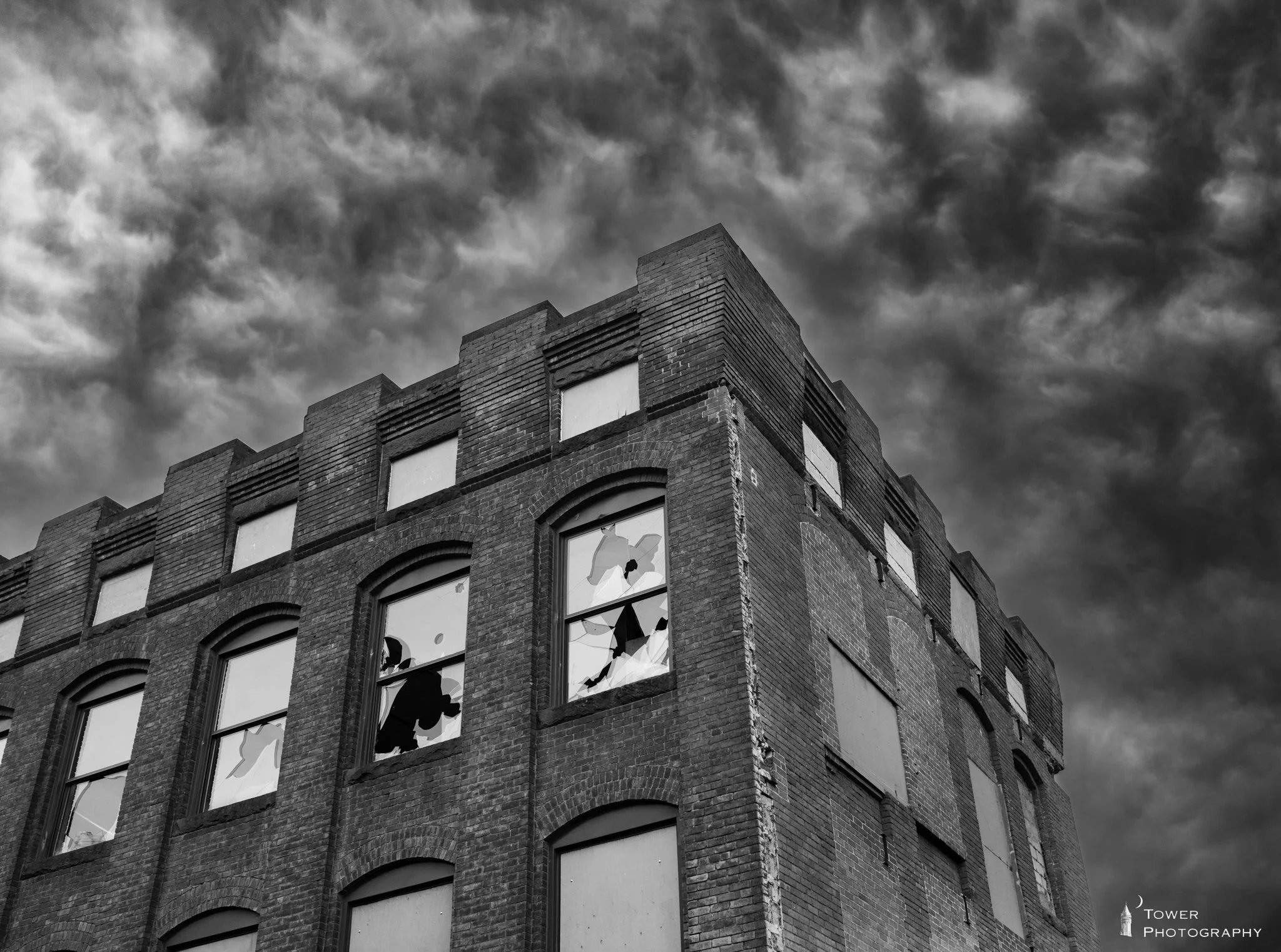 Black and white photo of an old brick building with broken windows against a dark, cloudy sky.