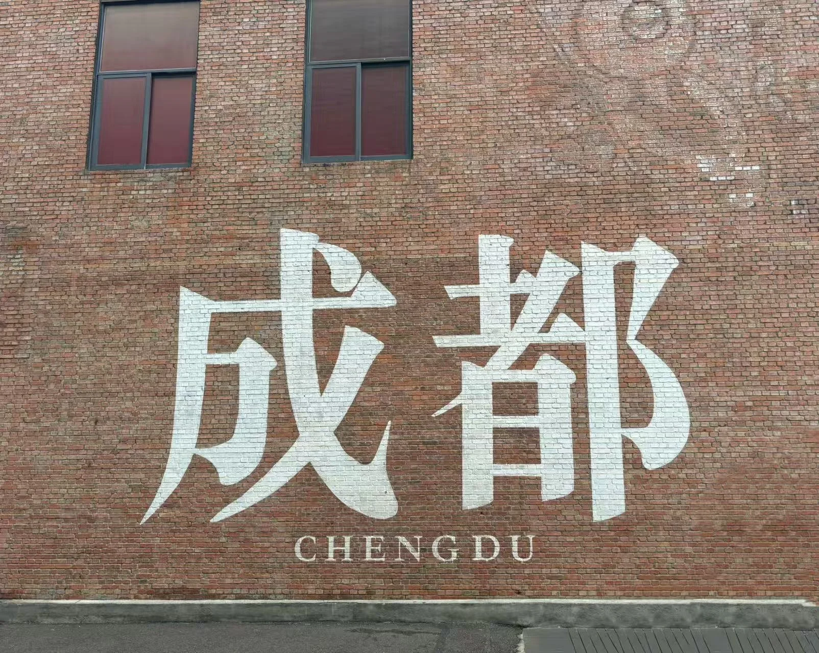 Large white Chinese characters on a red brick wall with small windows above, and the word 'CHENGDU' beneath.