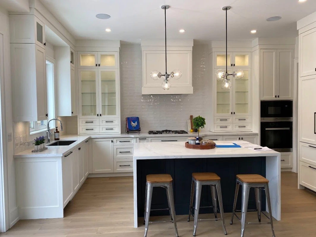 Modern kitchen with white cabinets, a central island with a dark base, three metal bar stools, pendant lighting, and a built-in oven.