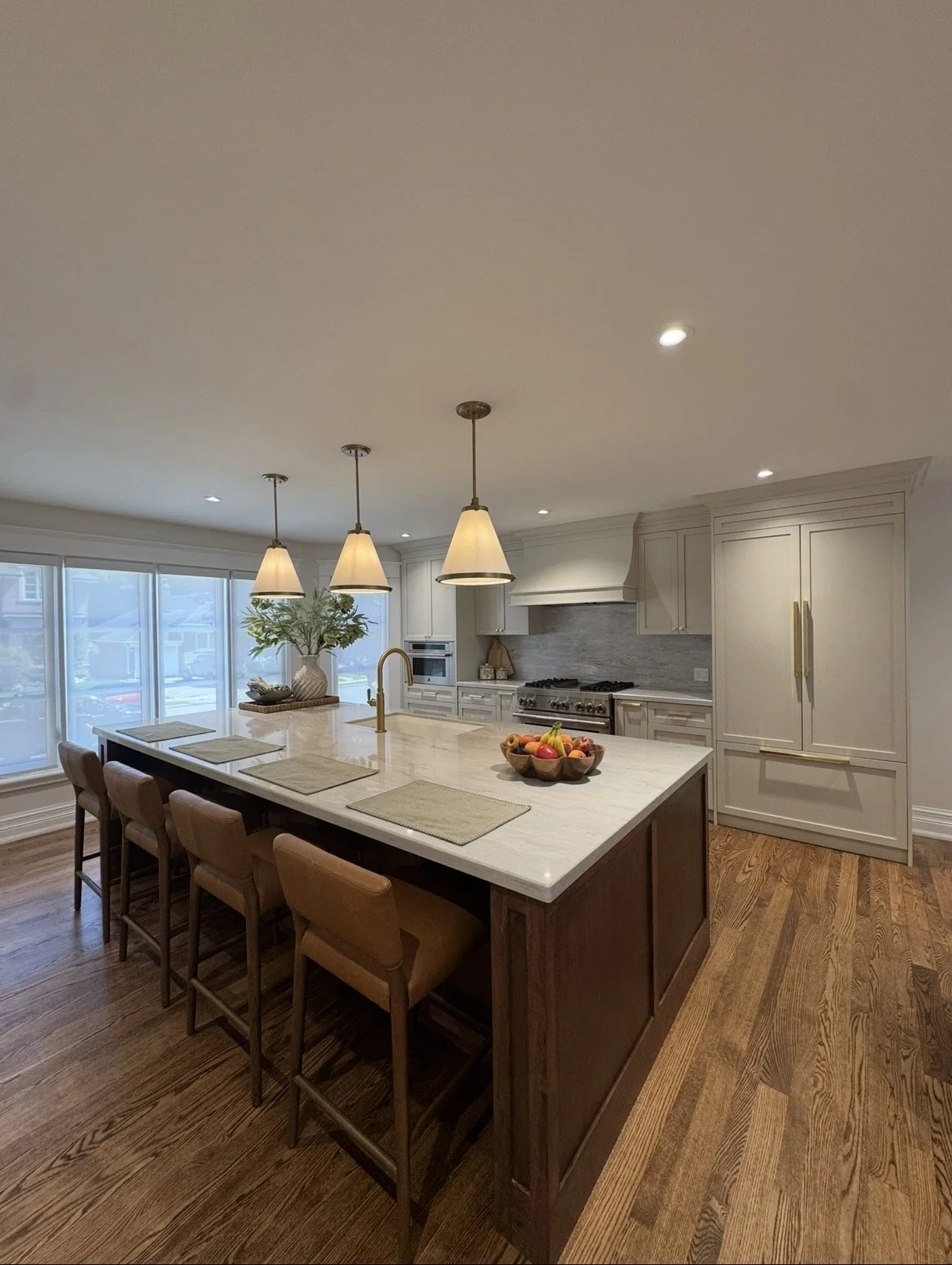 Modern kitchen with island, pendant lights, white cabinetry, stainless steel oven, bowl of fruit, and hardwood floors.