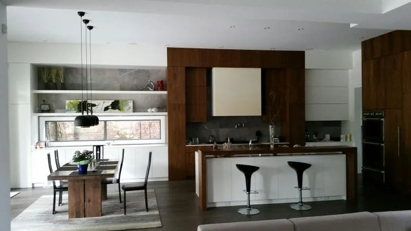 Modern kitchen with dark wood accents, a white island with two black bar stools, a dining table with four chairs, and a window providing natural light.
