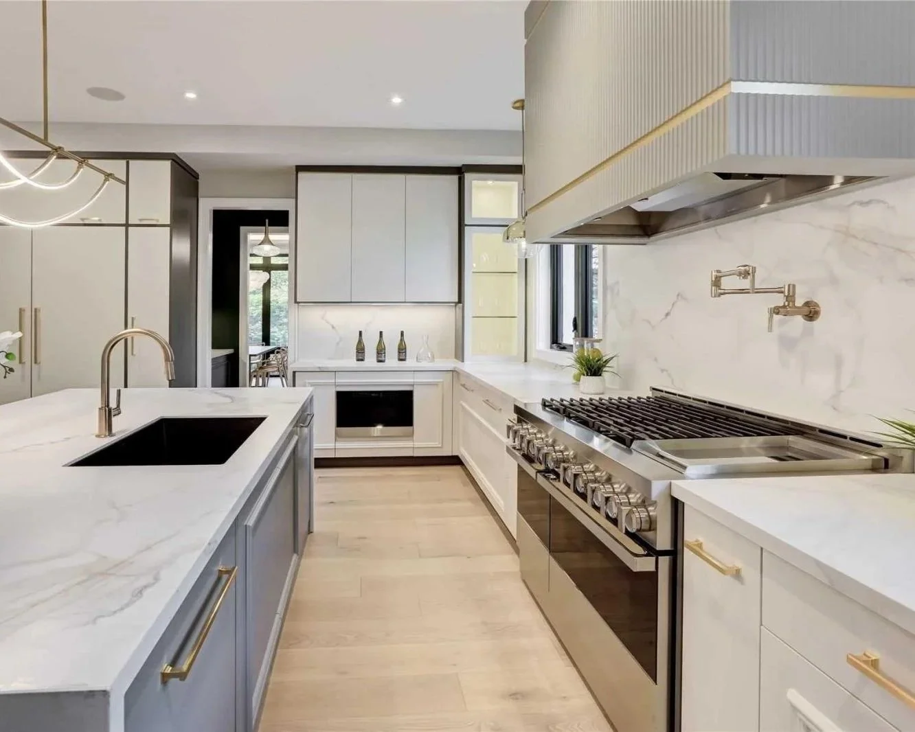 Modern kitchen with white marble countertops, a black sink, stainless steel stove, gold accents, and natural light from a window.