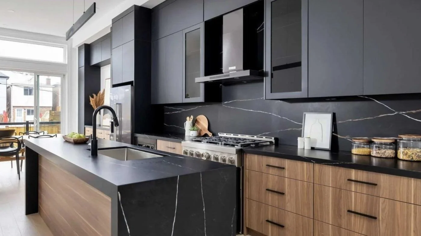 Modern kitchen with black and wooden cabinets, black marble backsplash, stainless steel stove, and a large window in the background.