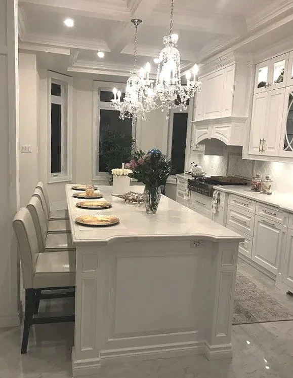 Elegant white kitchen with a large island, chandelier, and floral centerpiece.