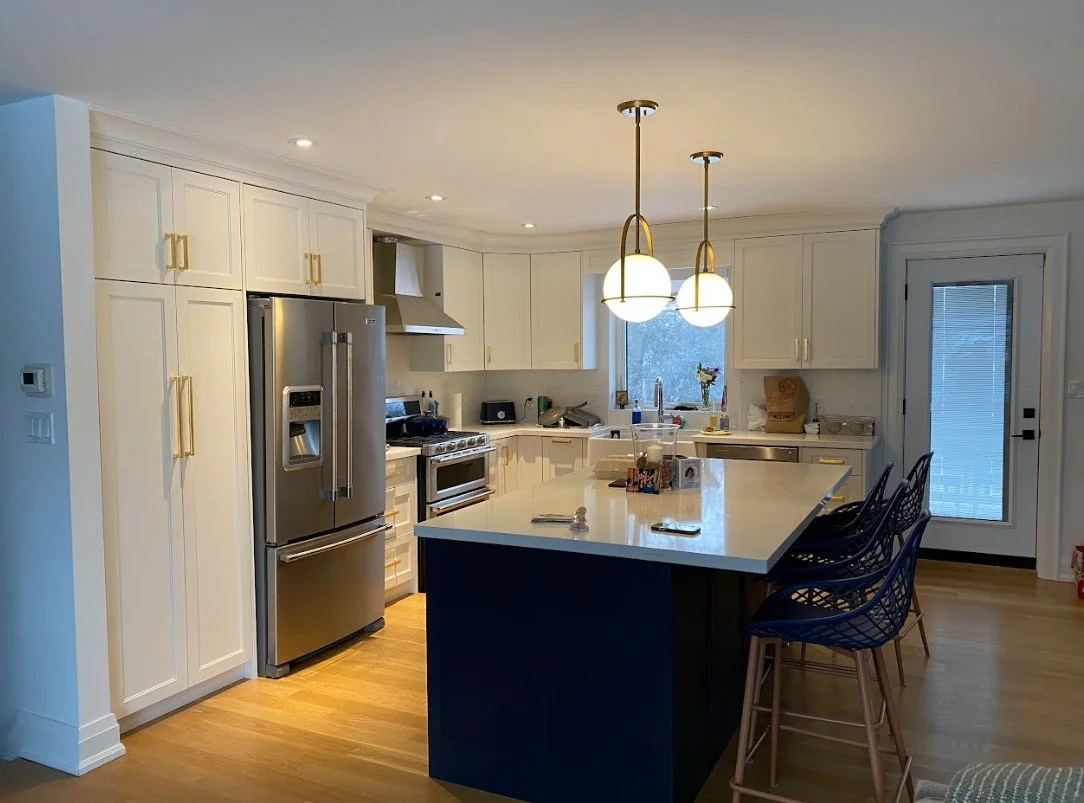 Modern kitchen with white cabinets, stainless steel refrigerator, stove, and dishwasher, island counter with black base, three black barstools, pendant lights, hardwood floor, window above sink, and a glass door.