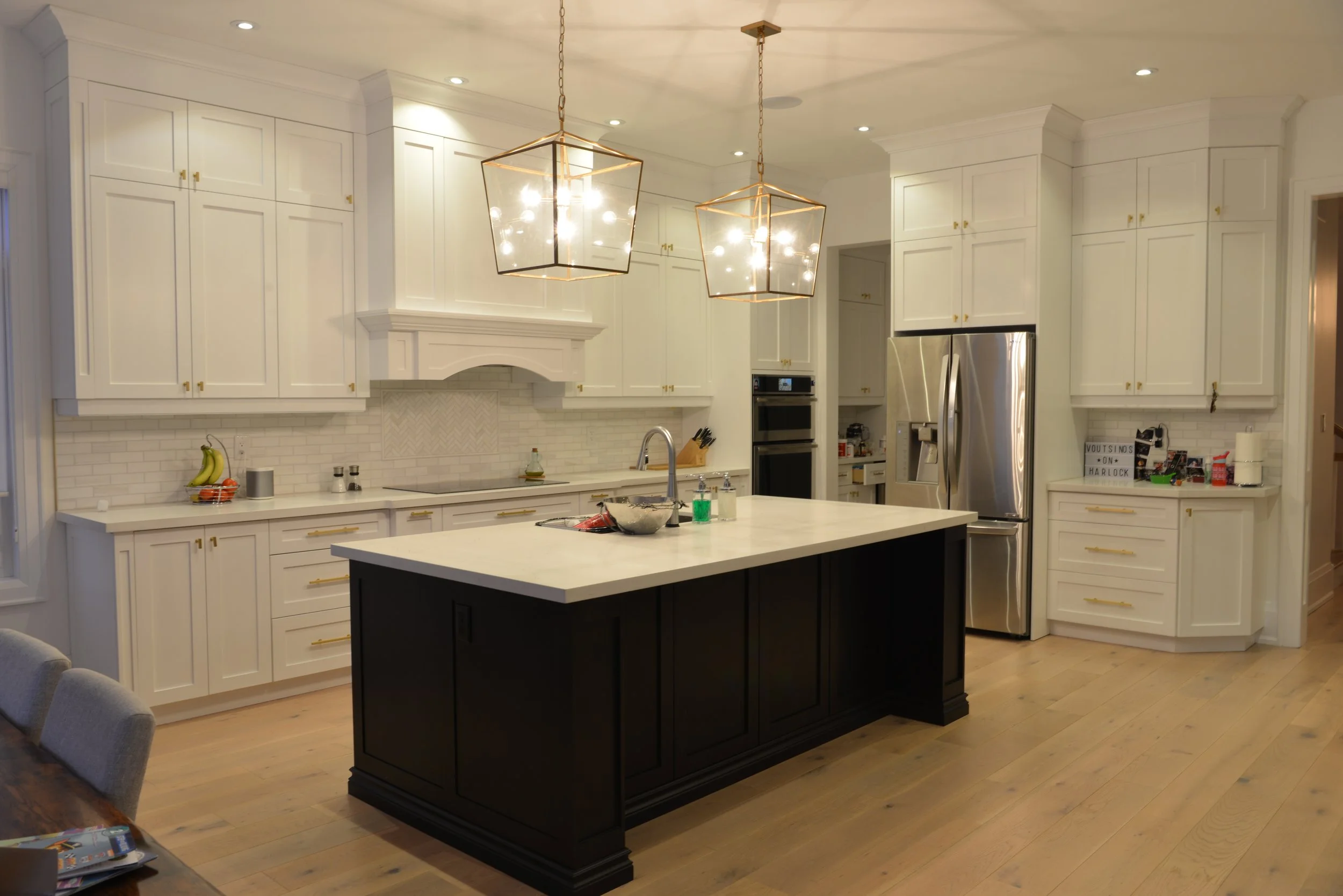 Modern white kitchen with a large island painted black, pendant lights, white cabinets, stainless steel refrigerator, and a brick backsplash.