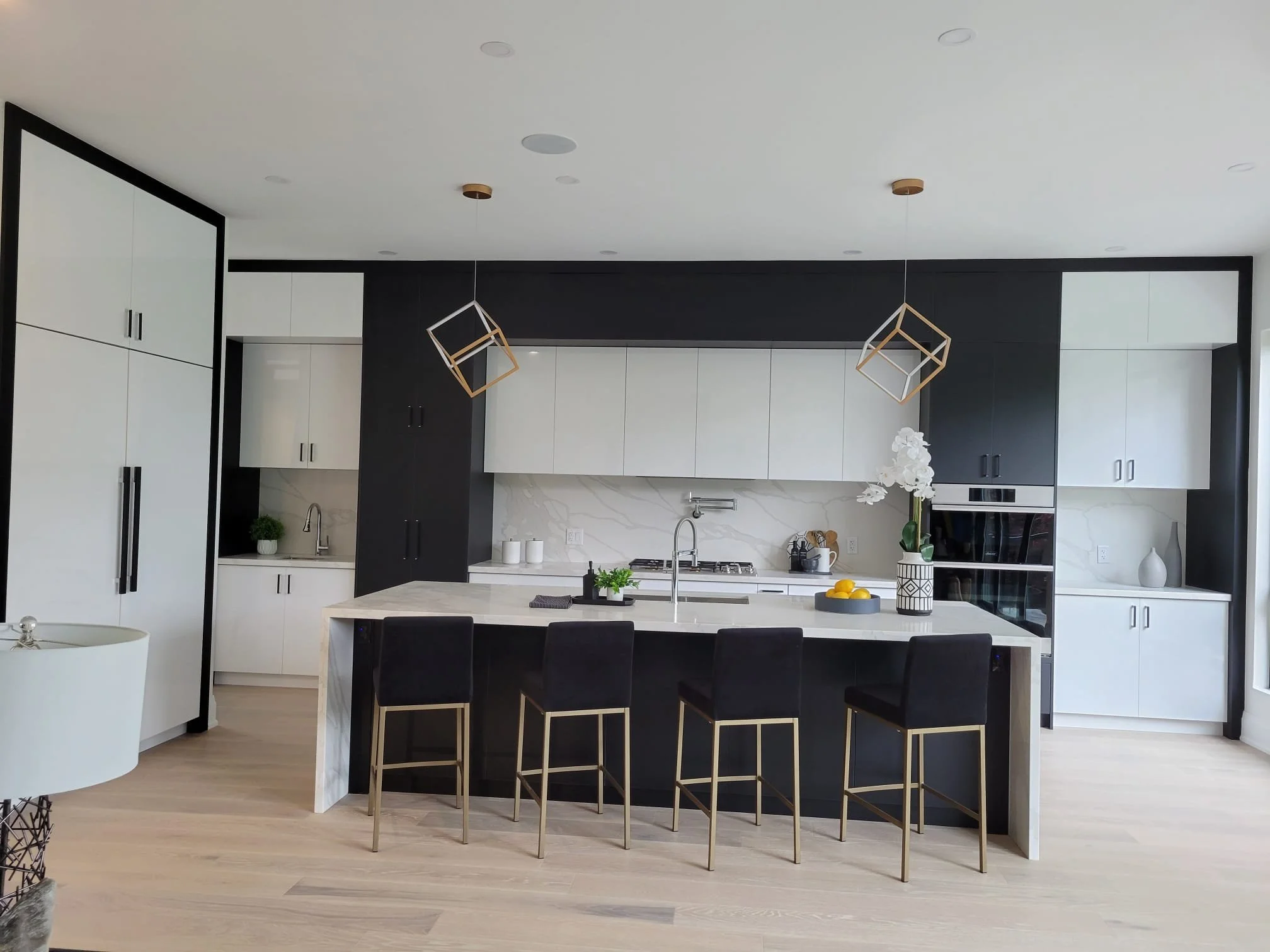 Modern kitchen with black and white cabinets, a large white island with seating, pendant lighting, and decorative flowers on the counter.